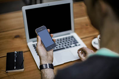 homme avec un smartphone dans la main devant un ordinateur